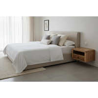 Beige upholstered bed with matching headboard and pillows next to chunky oak-ish floating bedside with single drawer and open shelf