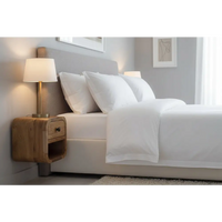 White bed with crisp linens and gray upholstered headboard next to extra mini curved oak-ish bedside with open slot