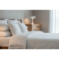A minimalist white bedside lamp with a dome shade on a wooden nightstand next to a large curved oak-ish chest opulent furniture