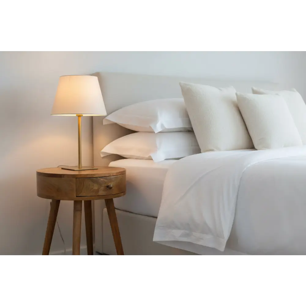 Minimalist nordic circular bedside table in wood with a single drawer and brass table lamp with beige shade