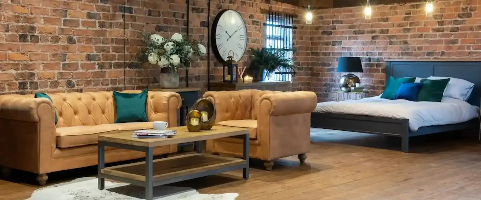 Living room with brown sofa, wooden coffee table, and bed with blue pillows against a brick wall.